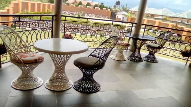 A balcony with a round table and two chairs, a second table with a chair, and a third table with a chair. - A & J Holiday Suites - Fort Portal (Bouvet Island)