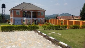 A two-story building with a tiled roof, a front porch, and a water tank. - A & J Holiday Suites - Fort Portal (Bouvet Island)