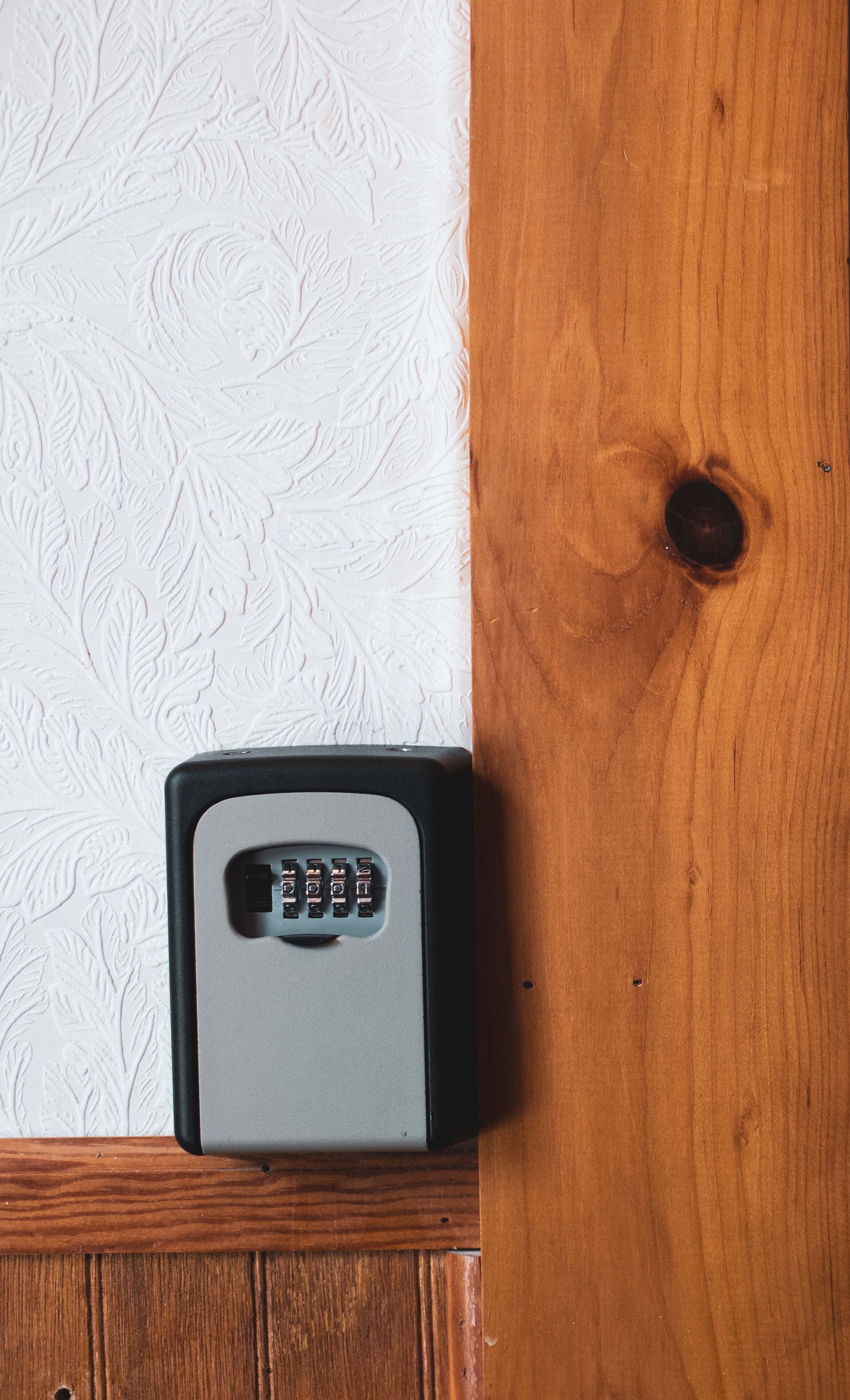 A small, gray, rectangular object with a keypad, placed on a wooden surface against a white textured wall.