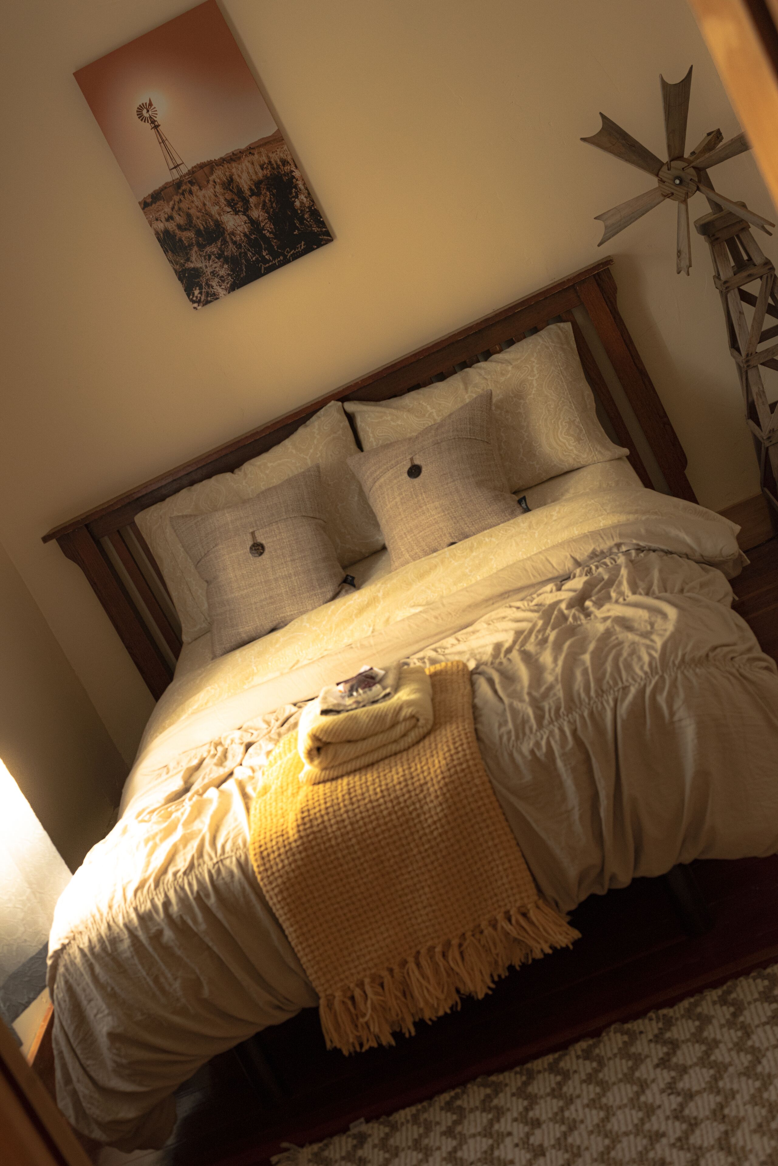 A neatly made bed with a headboard, a wall-mounted windmill picture, and a ceiling fan.