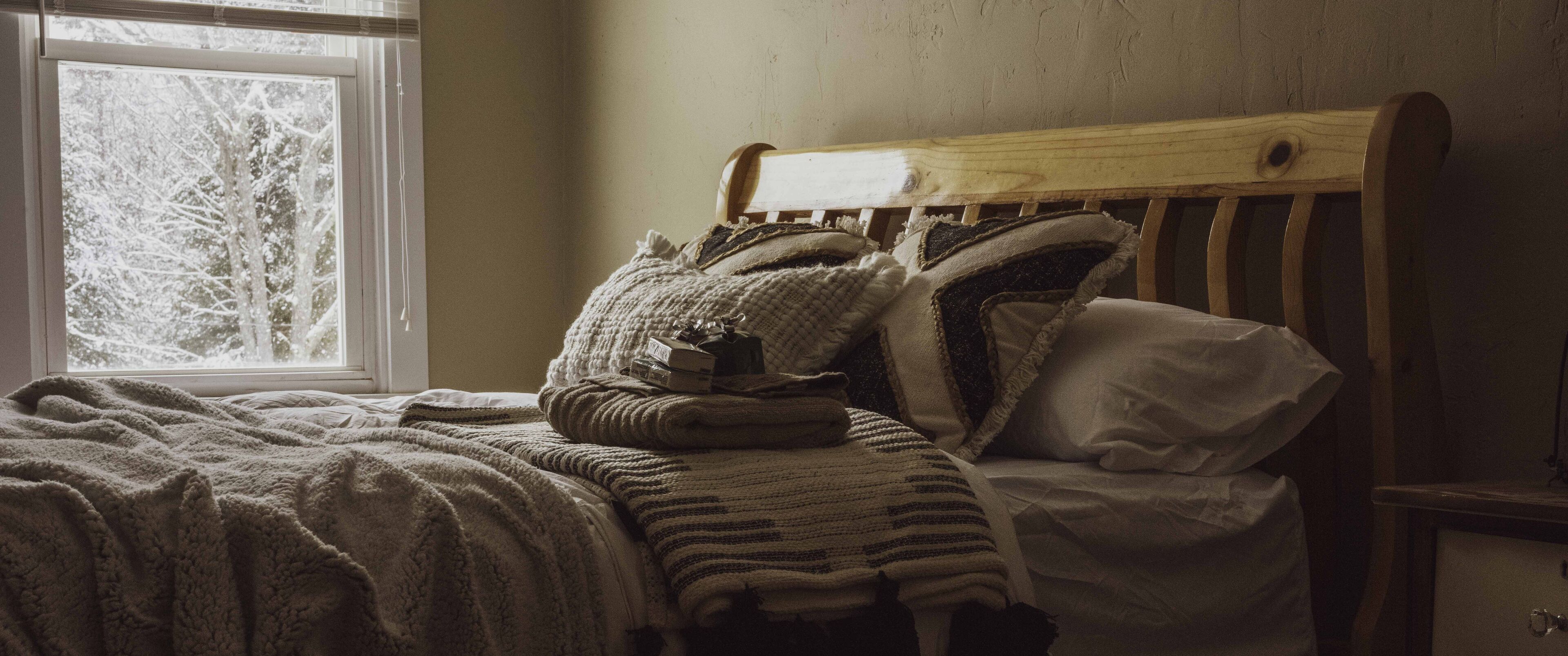 Una cama con cabecera de madera, varias almohadas y mantas.