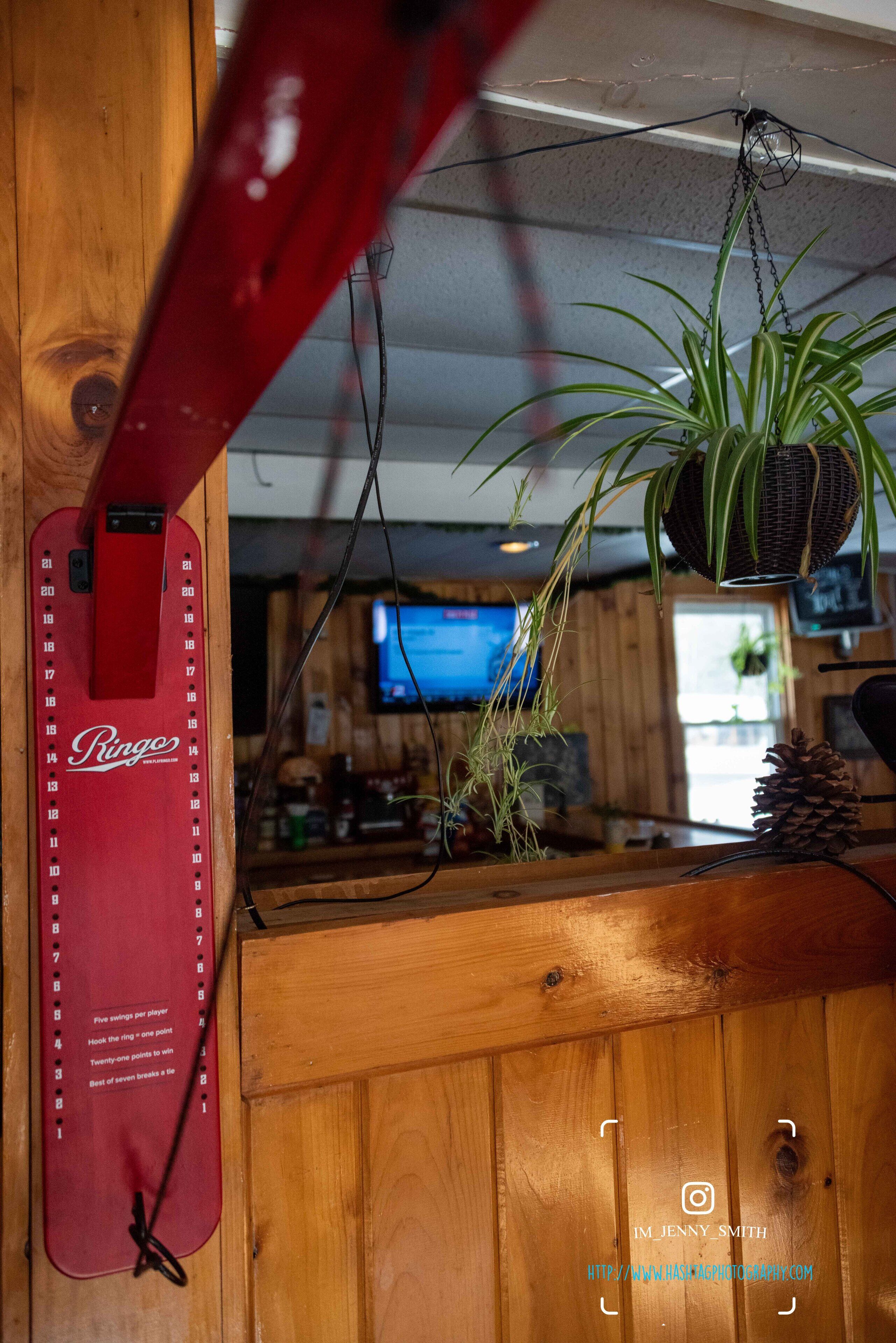Un mostrador de recepción de madera con un teléfono de marca Ringo rojo, una planta colgante y un televisor al fondo.