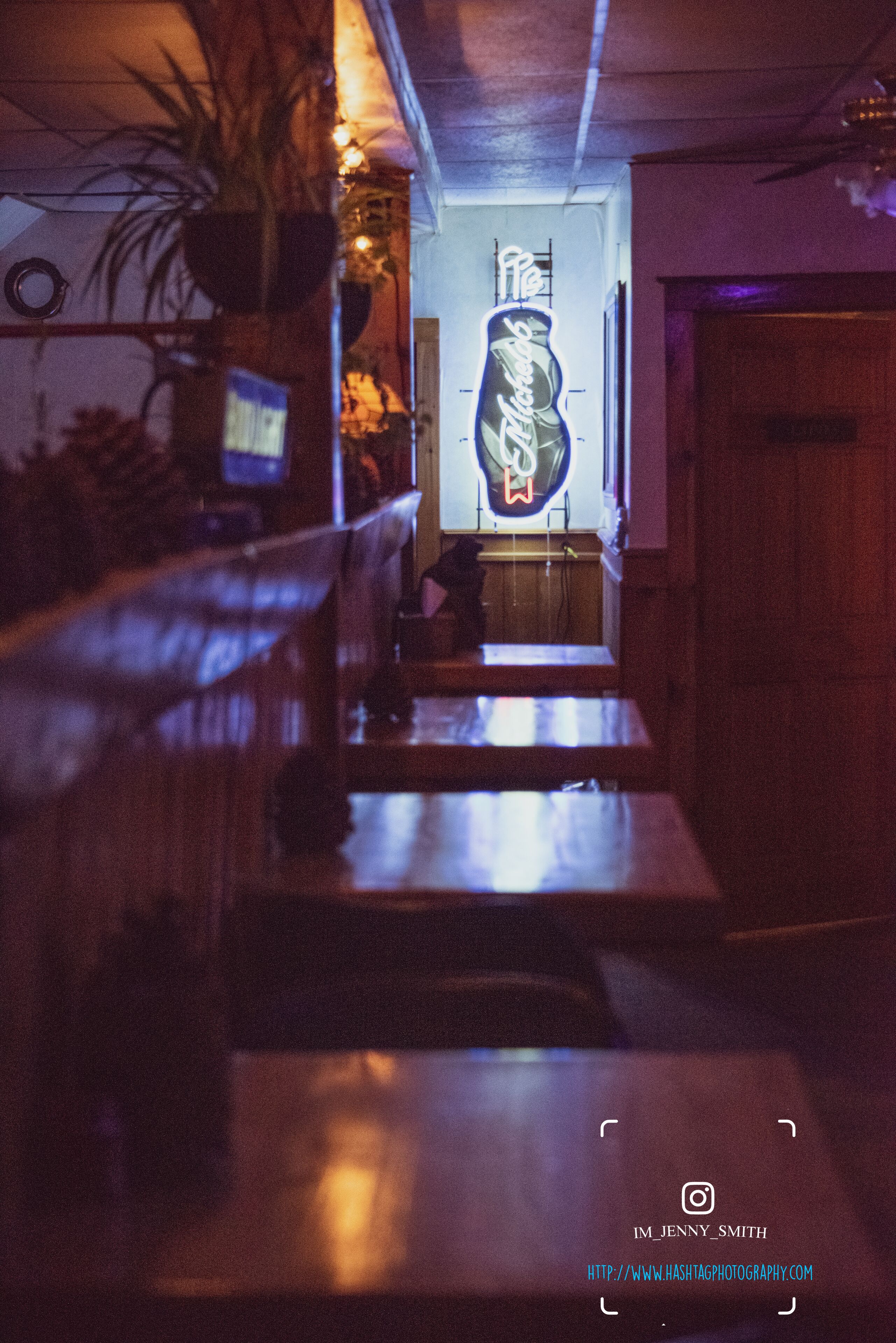 Un pasillo tenuemente iluminado con un letrero de neón, muebles de madera y una planta en maceta.