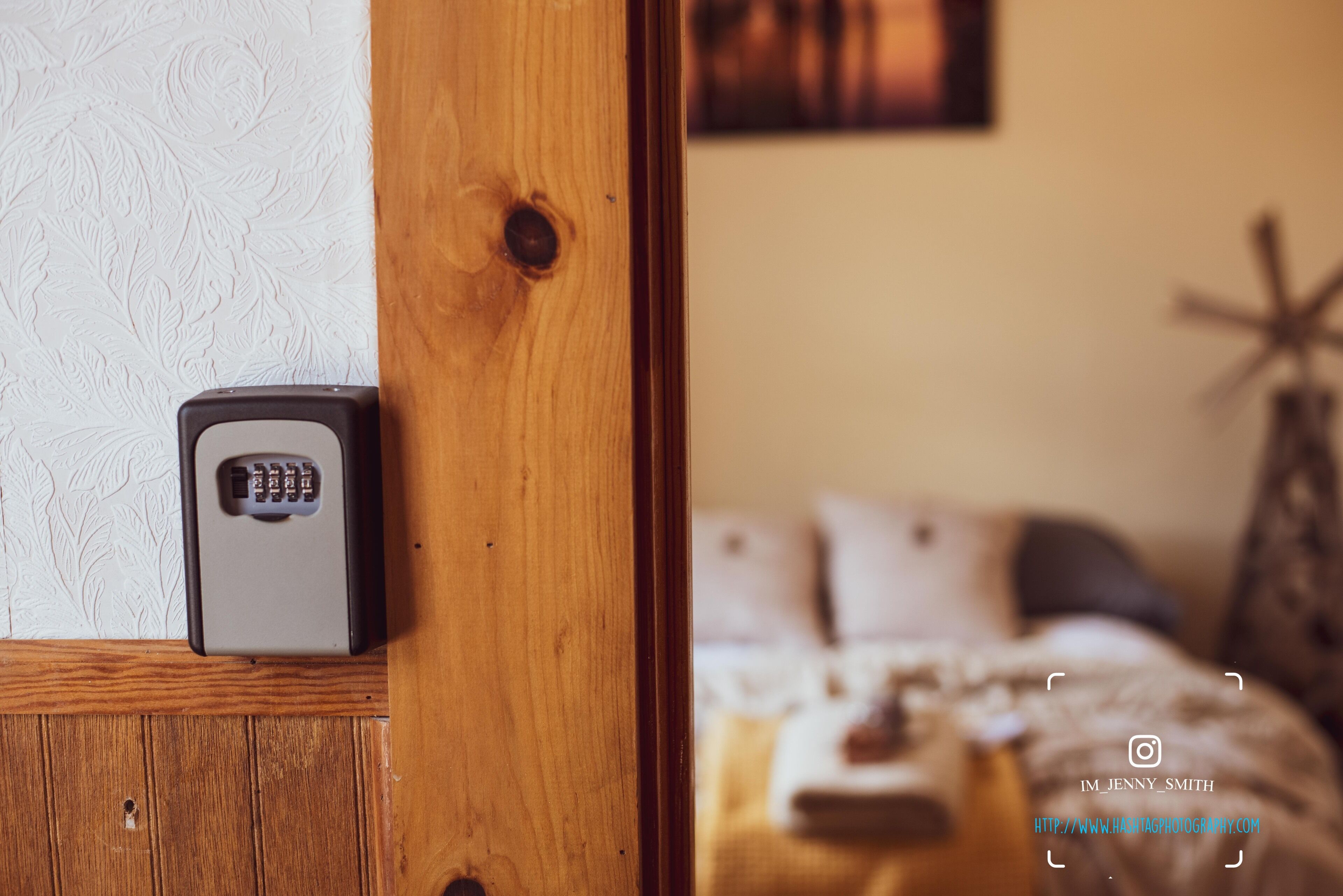 A wooden door with a security keypad, a bed with pillows, and a wall with a textured pattern.