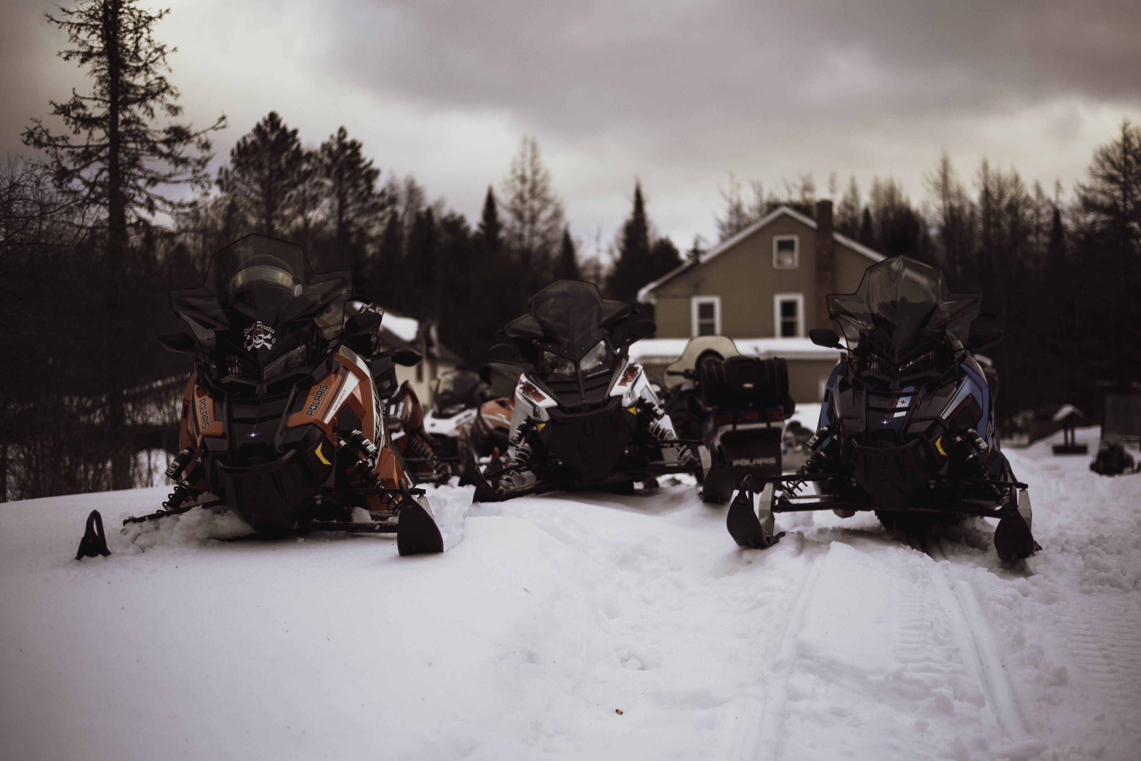 A group of snowmobiles parked in a snowy area with a house in the background.