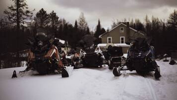 A group of snowmobiles parked in a snowy area with a house in the background.