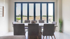 Comedor con una mesa y sillas, y vista a un jardín ajardinado a través de amplios ventanales.