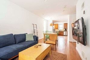 A modern living room with a sofa, coffee table, and a dining area with chairs and a table.