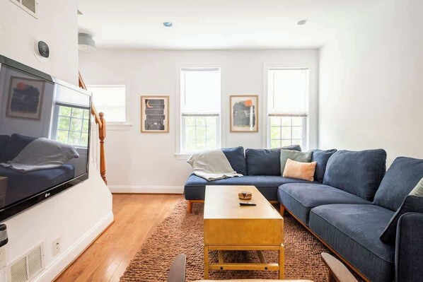 A modern living room with a large flat-screen TV, a blue sofa, a wooden coffee table, and a fireplace.
