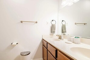 A modern bathroom with a white sink, wooden cabinets, a mirror, and towel rings.