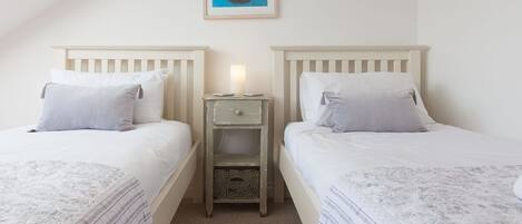 A twin room with two beds, a small bedside table with a lamp, and a framed artwork on the wall.