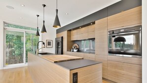 Une cuisine moderne dotée d’un îlot central, d’appareils électroménagers intégrés et de luminaires suspendus.