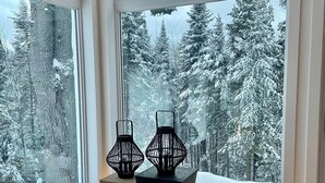 Une pièce dotée d’une grande fenêtre donnant sur une forêt enneigée. On y trouve deux lampes décoratives noires posées sur une petite table d’appoint en bois.