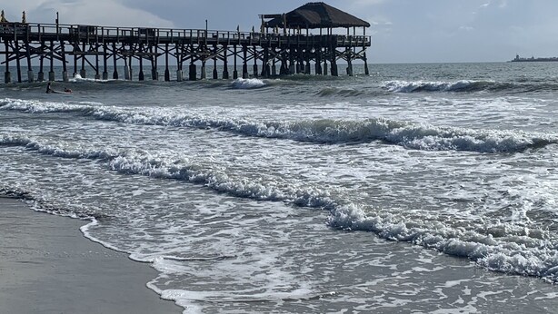 A beach with a pier extending into the ocean, featuring a covered seating area.