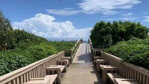 A long wooden boardwalk with benches on both sides, leading towards a distant view.