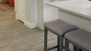 A modern kitchen with white cabinets, a grey countertop, and a bar stool.