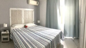 A small, neatly made bed with a patterned bedspread, a bedside table with a lamp, and a window with curtains. - ON THE Caribbean SEA - Crystal Apartment (Boca Chica)