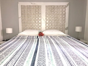 A hotel room with a patterned bedspread, two white pillows, a decorative wall panel, and bedside lamps.