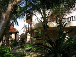 A two-story building with a balcony, surrounded by tropical vegetation.
