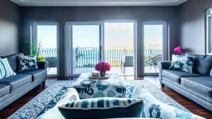 A modern living room with a large sliding glass door leading to a balcony with a view of the sea.
