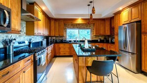 A modern kitchen with wooden cabinets, stainless steel appliances, a central island, and a large window.