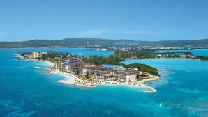 An aerial view of a resort island with multiple buildings, a beach, and clear blue waters.