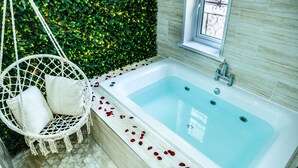 Une salle de bain moderne avec une baignoire blanche, un fauteuil suspendu avec des coussins et un mur végétal verdoyant.