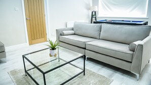 Un salon comprenant un canapé, une table basse en verre, une plante en pot, une table de billard et une porte.