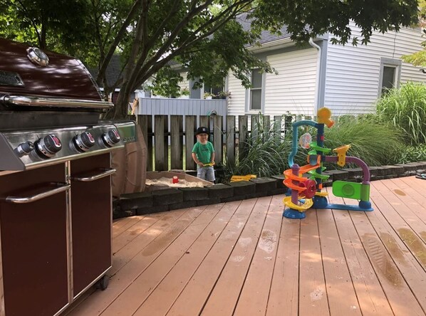 A barbecue grill, a wooden deck, and a play structure. - Cozy home, minutes from lakeshore! (Spring Lake)