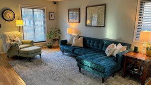 Una sala de estar con un sillón verde, un sofá azul, suelo de madera y un ventilador de techo.