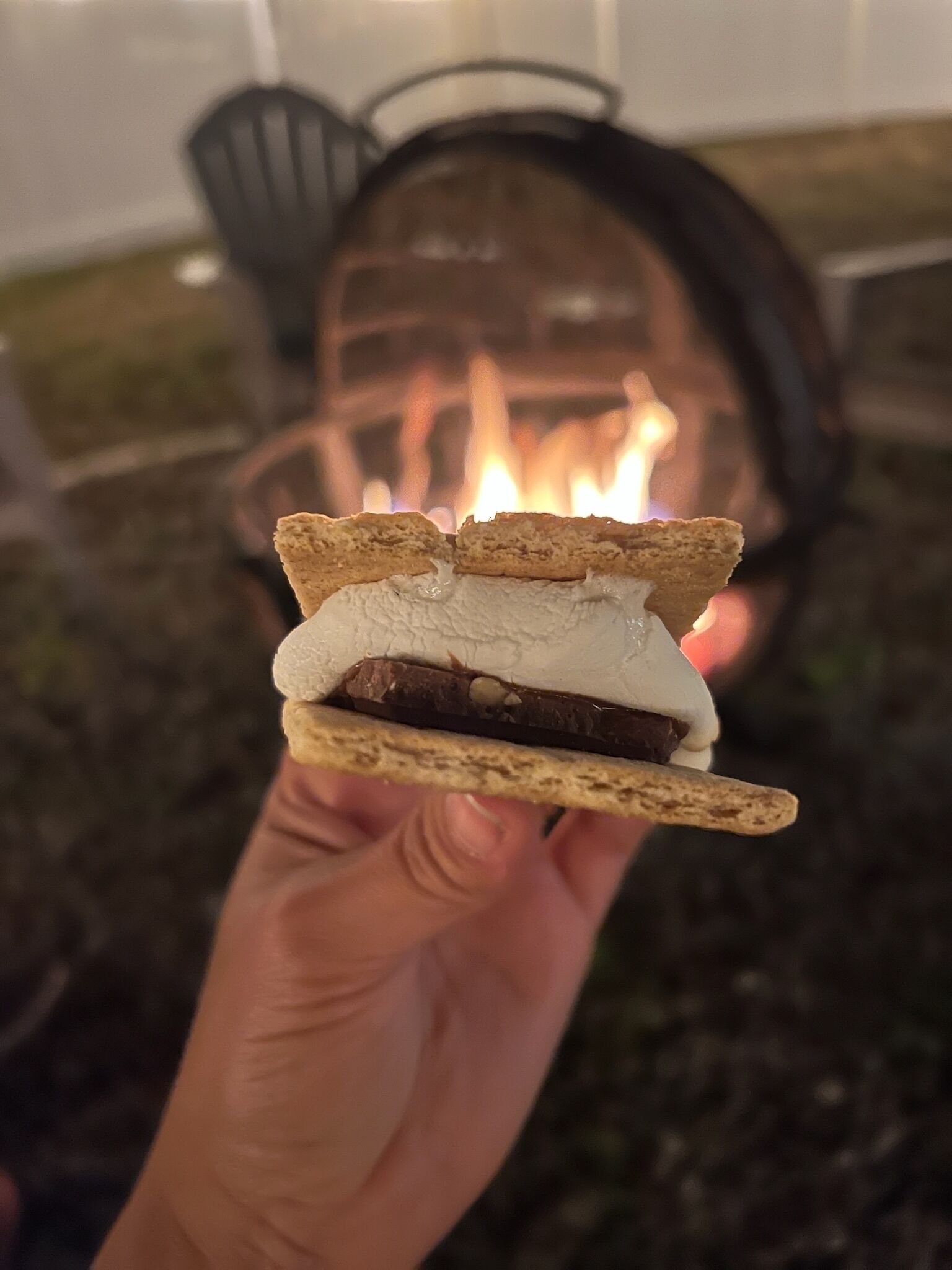 Eine Hand hält einen S'more mit Marshmallows und Schokolade zwischen Graham Crackern.