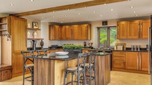 A spacious kitchen with wooden cabinets, a central island with bar stools, and a window providing natural light. - Hilltop View with Hot Tub (Brecon)