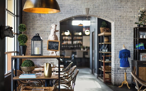 Ein Restaurantinneres mit Ziegelwänden, Korbmöbeln, einer Kreidetafel und einer Schaufensterpuppe in einem blauen Hemd.