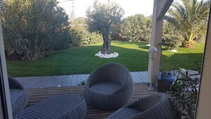 Ein überdachter Patio-Bereich mit Korbmöbeln und Blick auf einen gepflegten Rasen und Bäume.