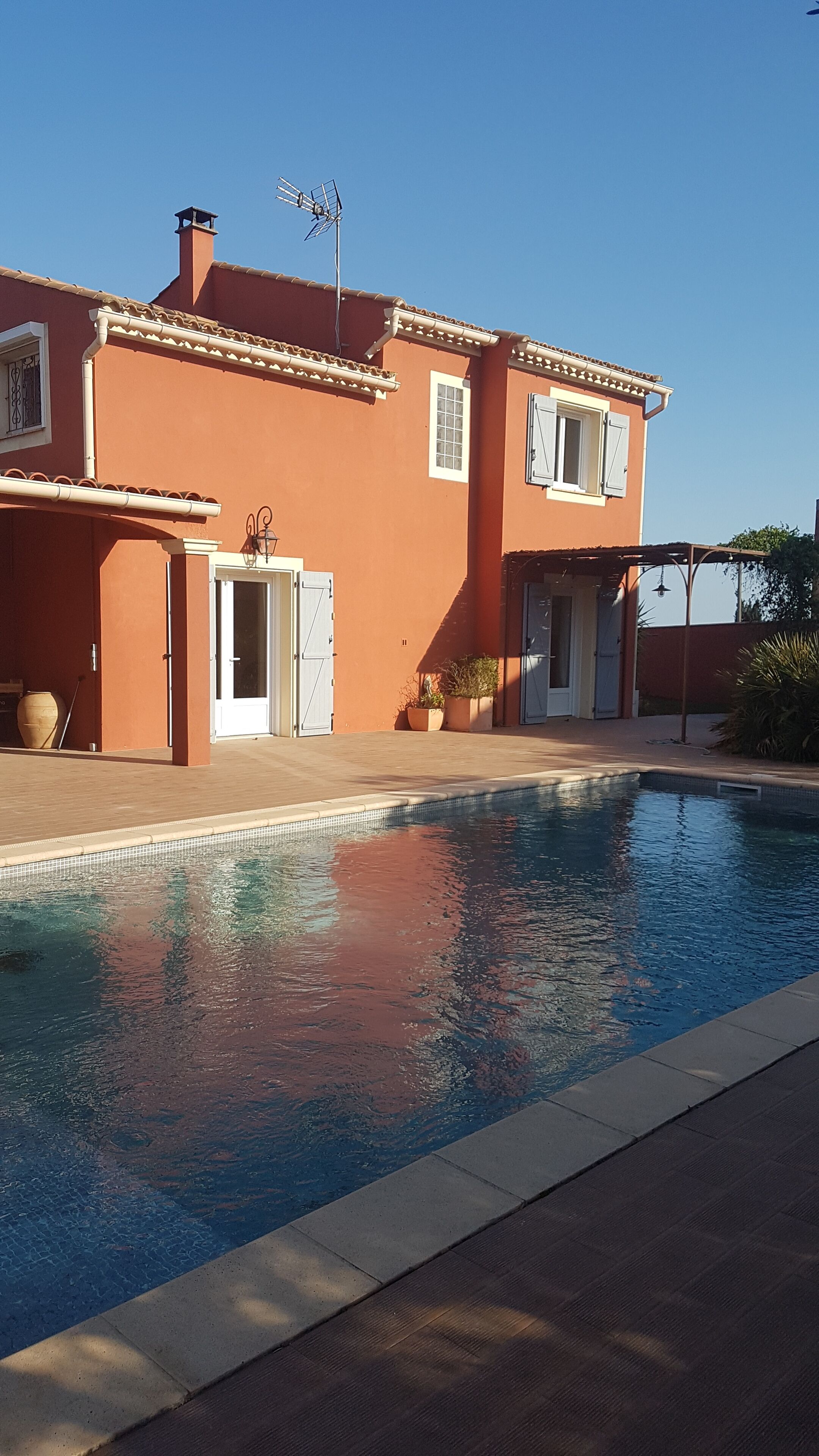 A house with a swimming pool, a covered patio, and a clear blue sky.