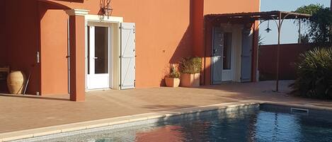 A house with a swimming pool, a covered patio, and a clear blue sky.