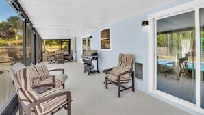 A covered patio area with striped chairs, a grill, and a pool view. - Relax and Unwind in 2 BR apt with Private Heated Pool (Sebastian)