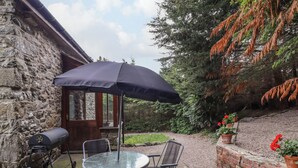 A patio with a round table and chairs, a black umbrella, and a stone wall. - Yr Hen Felin (Oswestry)
