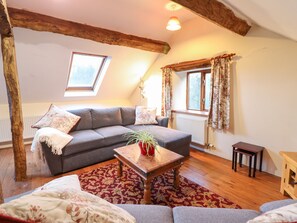 A cozy living room with a grey sofa, a wooden coffee table with a plant, a red rug, and a wooden floor.