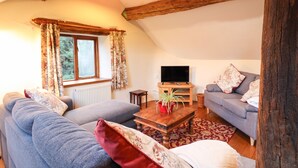 A cozy living room with a wooden ceiling, a sofa, a loveseat, a coffee table, and a television. - Yr Hen Felin (Oswestry)