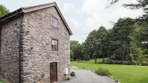 A stone building with a gravel driveway leading to a wooden gate, surrounded by lush greenery and trees. - Yr Hen Felin (Oswestry)
