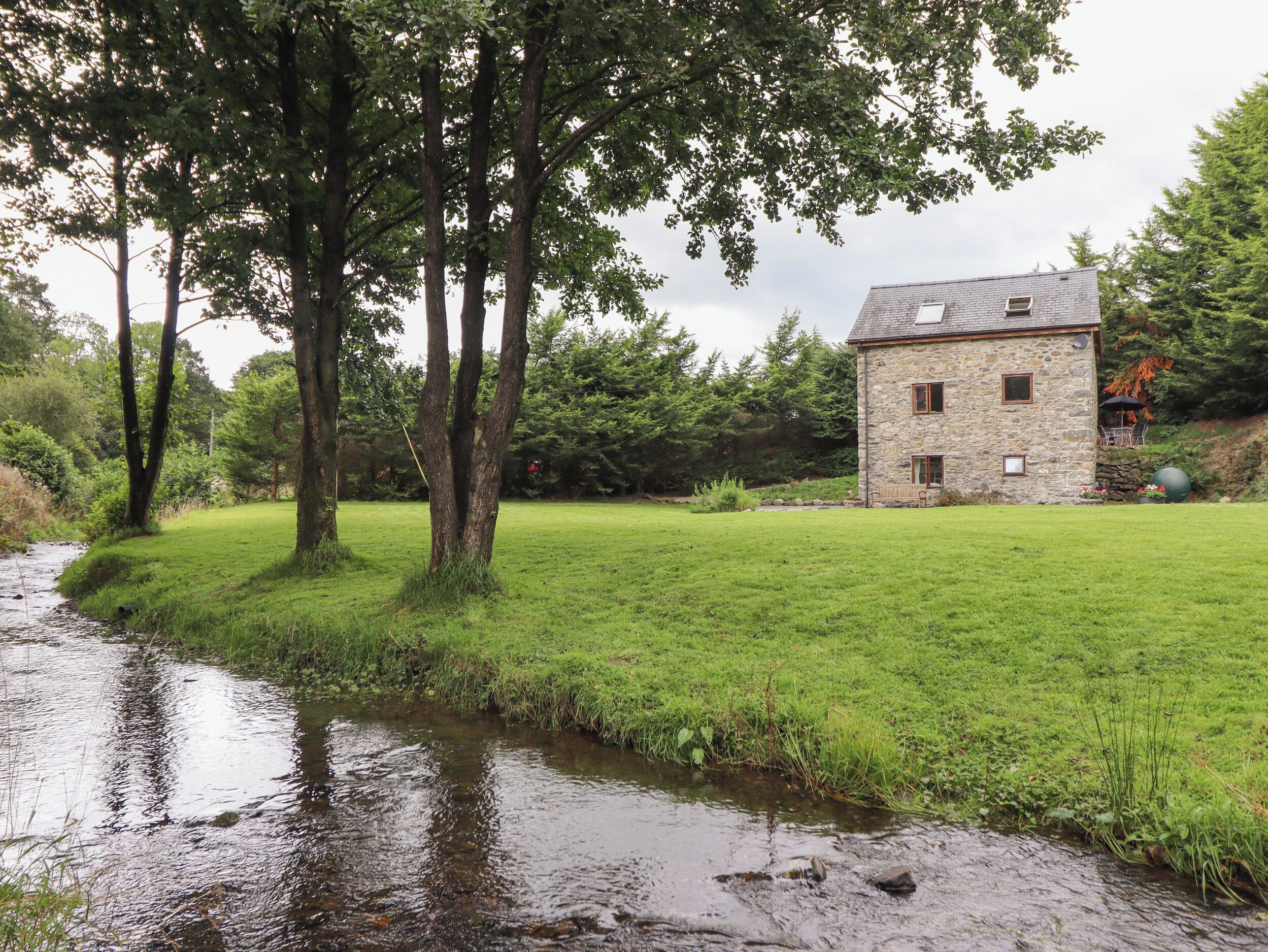 A stone house with a grassy yard and a stream.