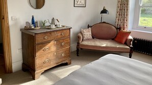 A bedroom with a wooden dresser, a bed, a chair, a window with curtains, and a framed picture on the wall. - Frizenham Farmhouse B&B (Torrington)