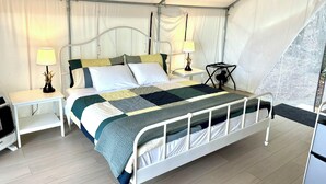 Ein Zeltraum mit Bett, Nachttischen, Lampen und einem Ventilator.