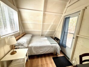Une petite chambre confortable, avec un lit simple, une table de chevet avec une lampe, une fenêtre avec des stores et une vue sur l’extérieur.