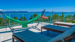 A balcony with a hammock, two lounge chairs, and a view of the sea and mountains. - Villa with exceptional views (Labin)