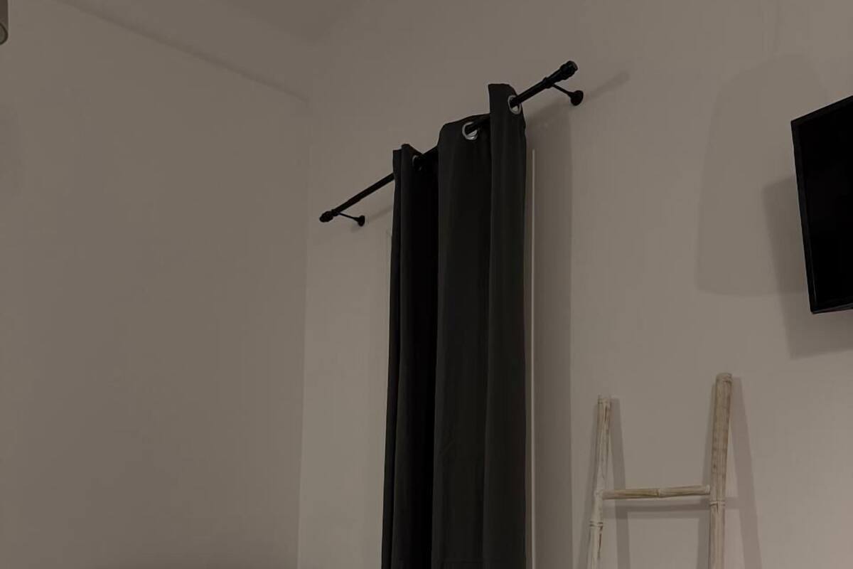 A bedroom with a bed, a black curtain, a ladder, and a wall-mounted TV.