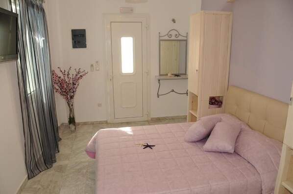 A bedroom with a bed, a wardrobe, a mirror, and a door. - Starlight Luxury Studios (Mykonos)