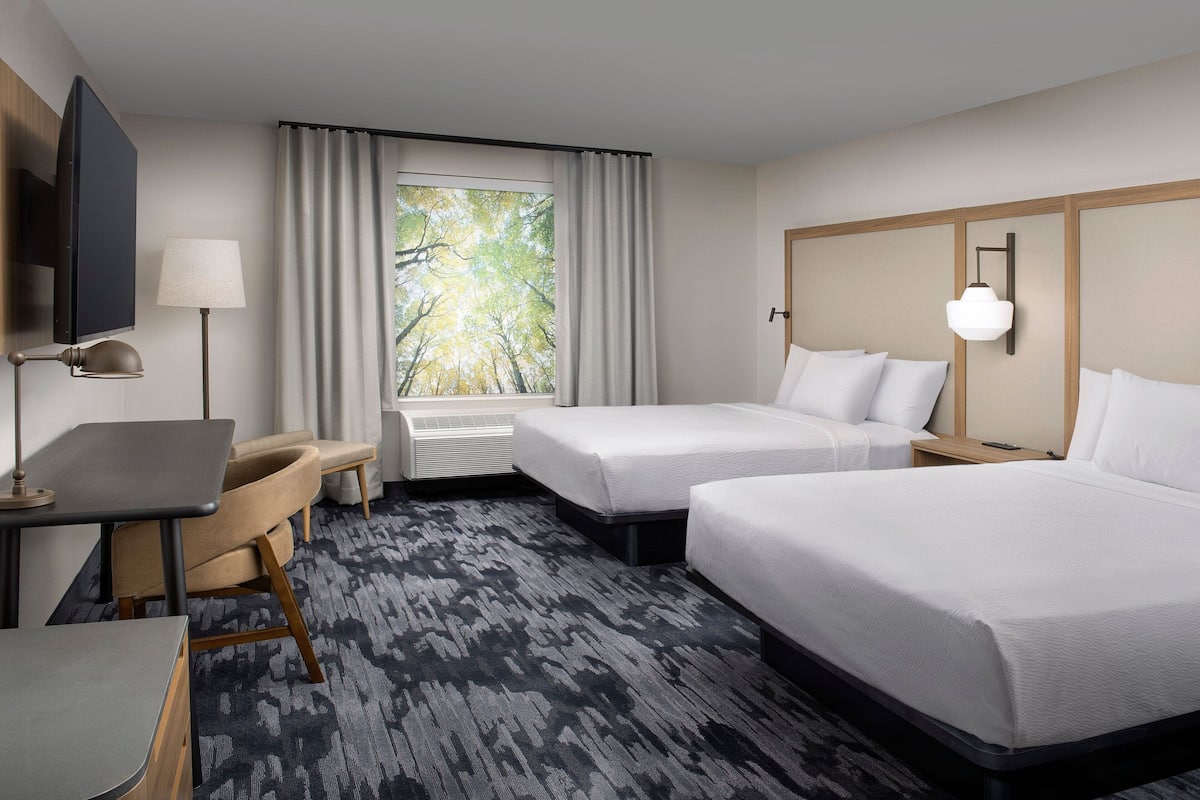A hotel room with two beds, a desk, a chair, a TV, and a window with curtains.