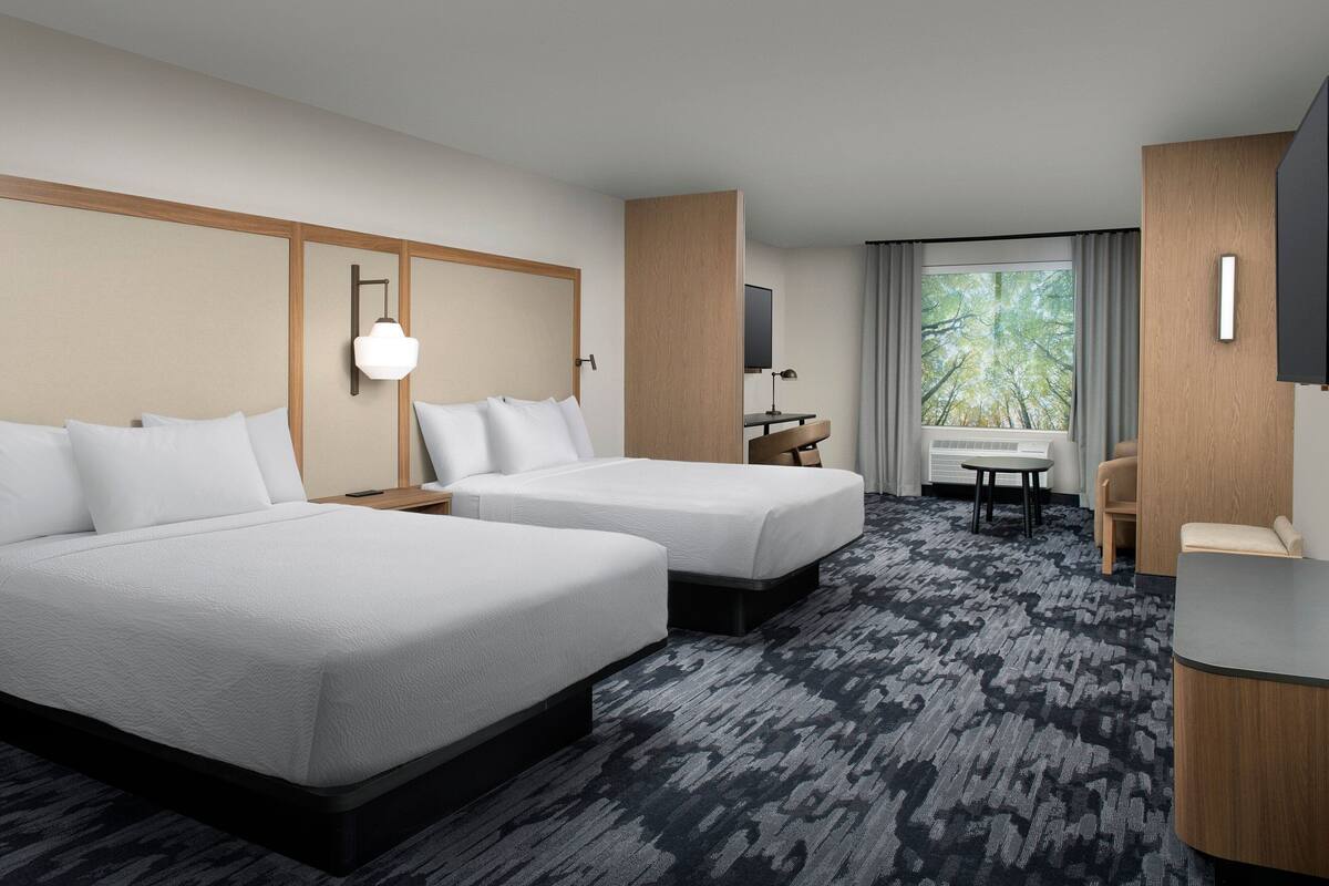 A hotel room with two beds, a desk, a chair, and a large window with curtains.